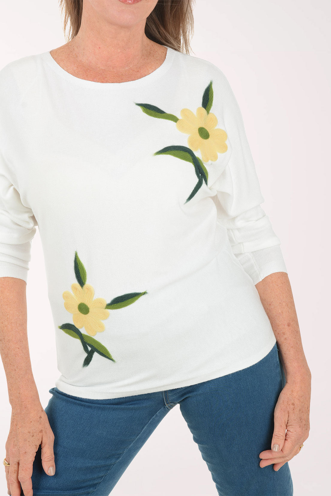 Woman wearing a white sweater with floral designs on a plain background