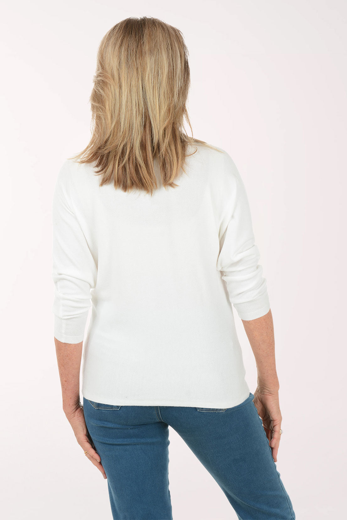 Woman wearing a white sweater with floral designs on a plain background