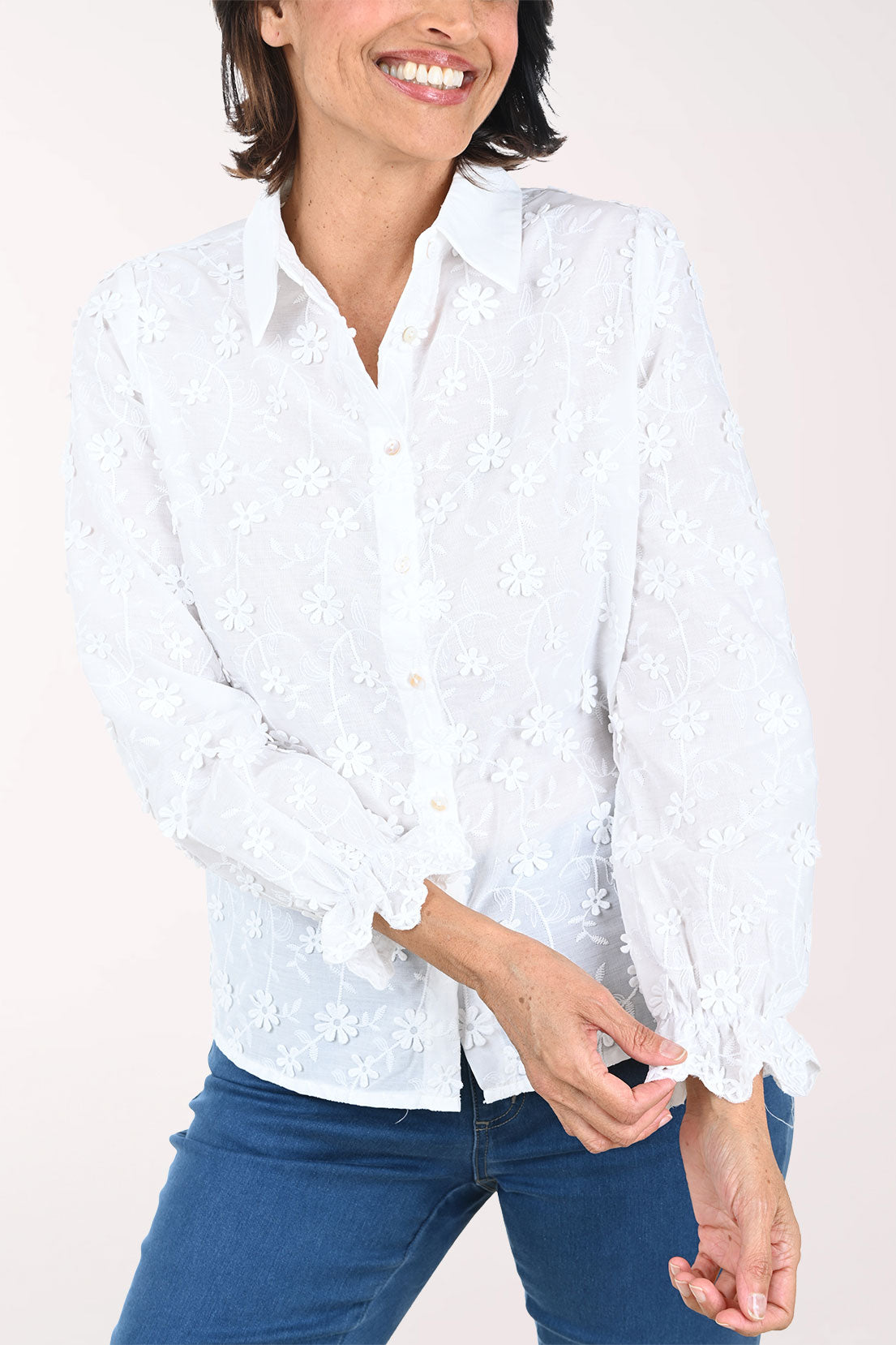 Woman wearing a white patterned shirt and blue pants on a white background