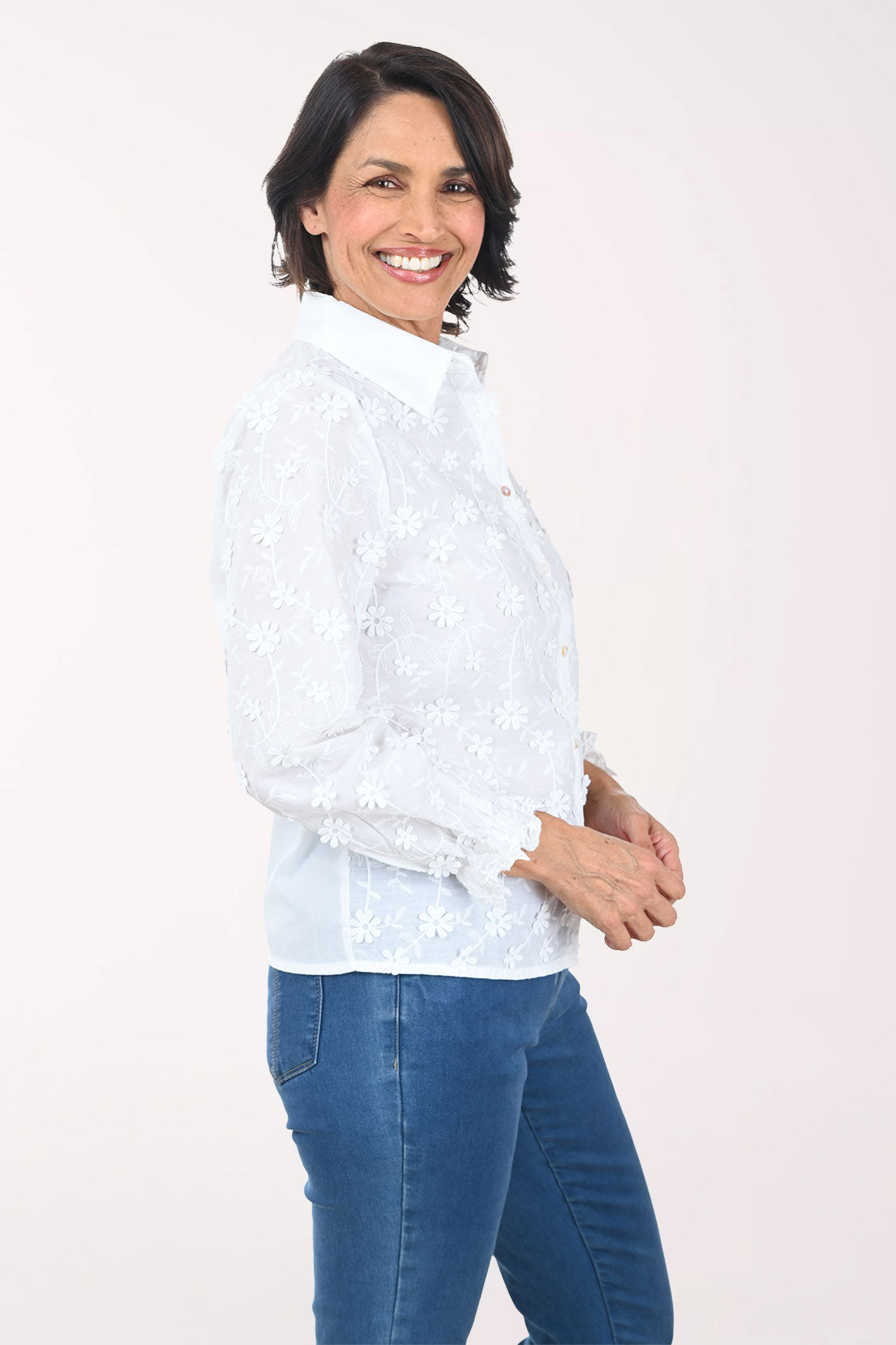 Woman wearing a white patterned shirt and blue pants on a white background