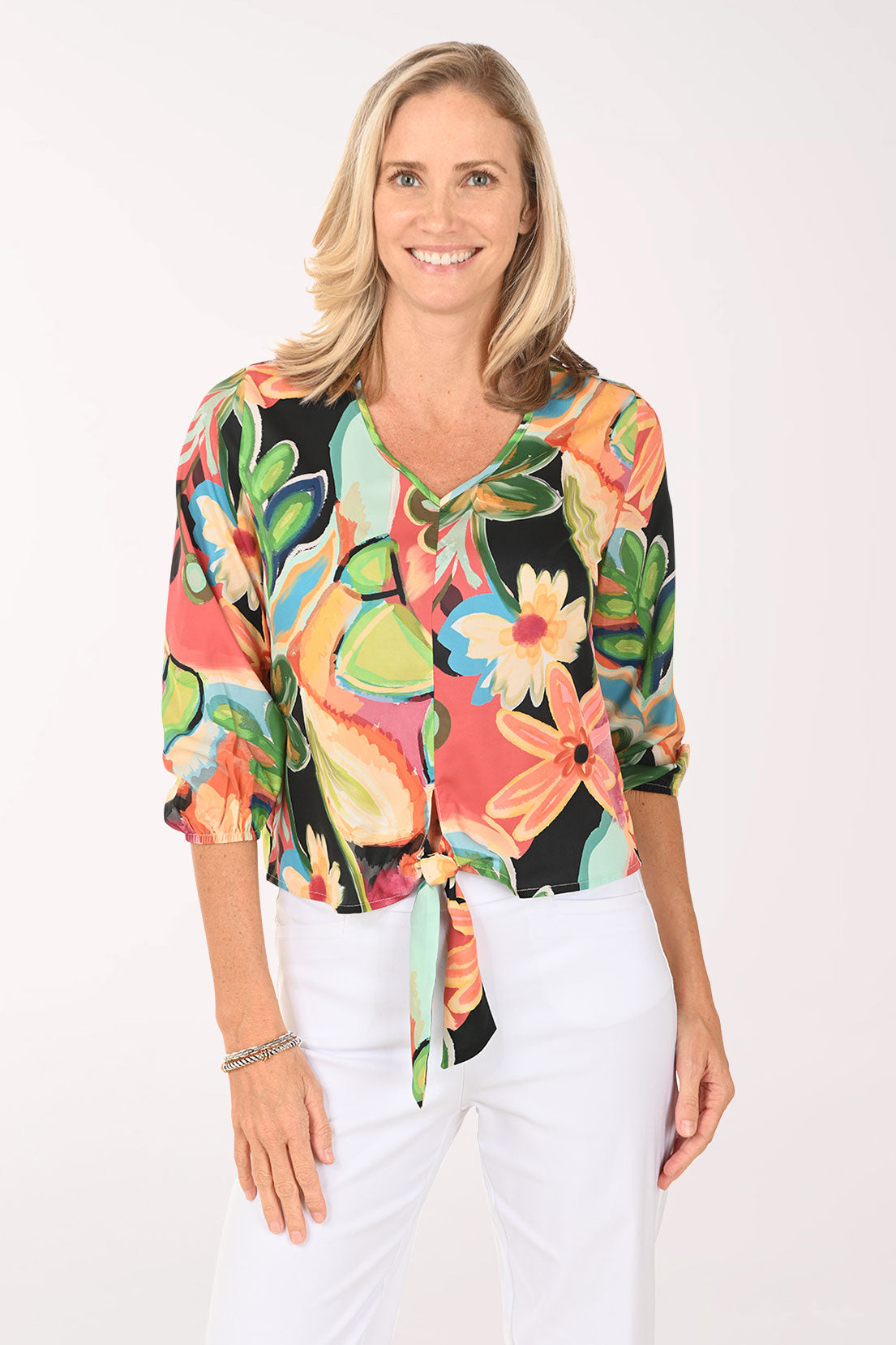 Woman wearing a v-neck multi colored top with a tie at the hemline.