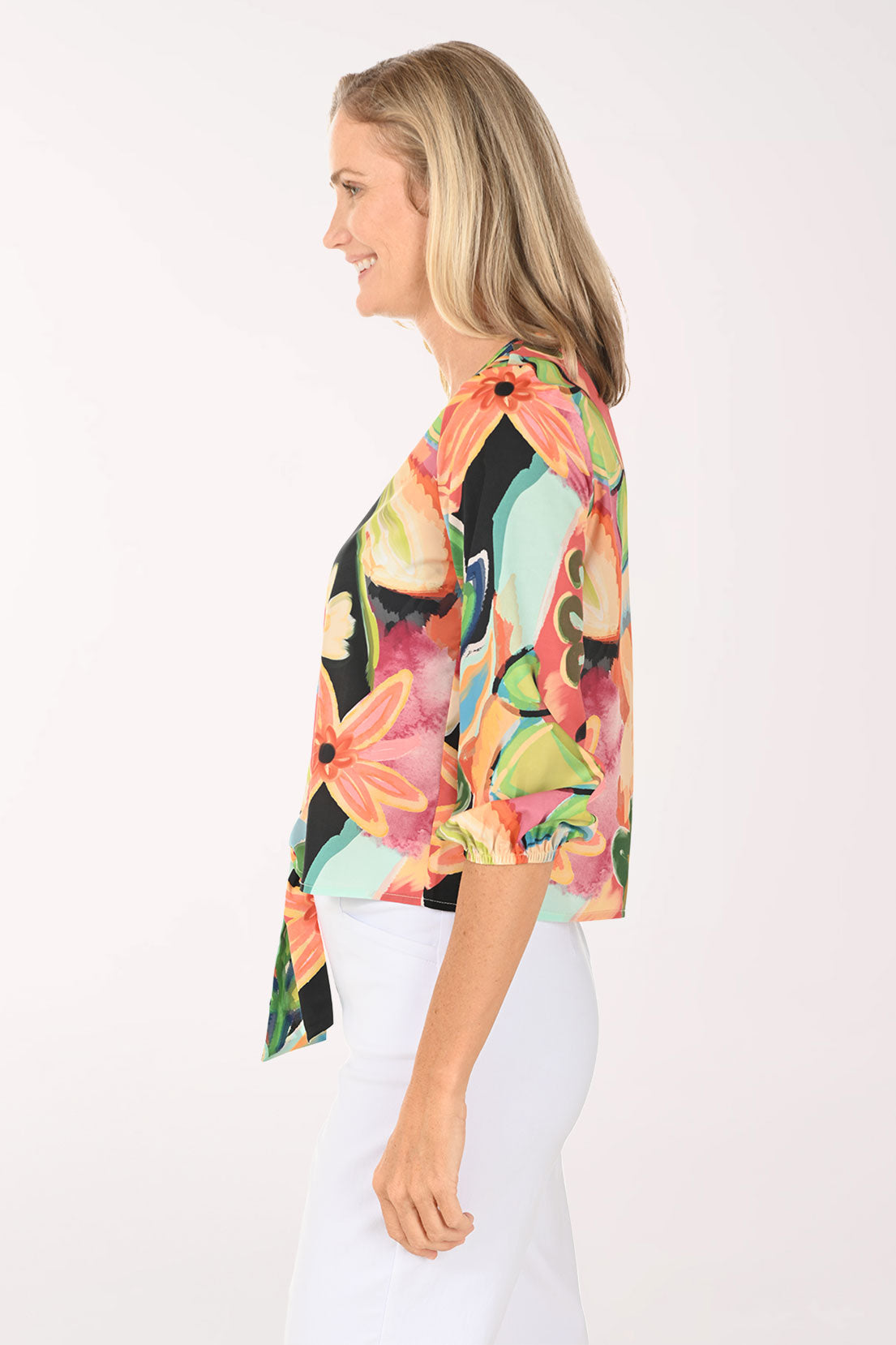 Woman wearing a v-neck multi colored top with a tie at the hemline.