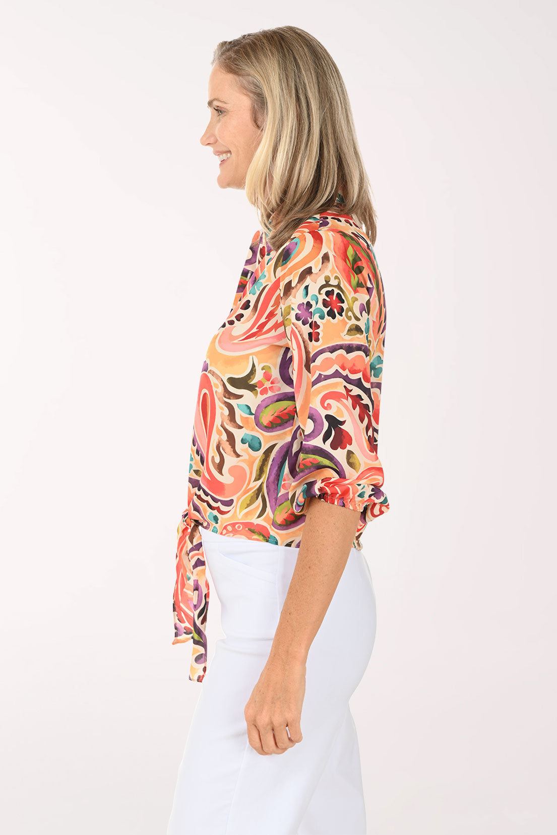 Woman wearing a colorful paisley blouse and white pants on a white background