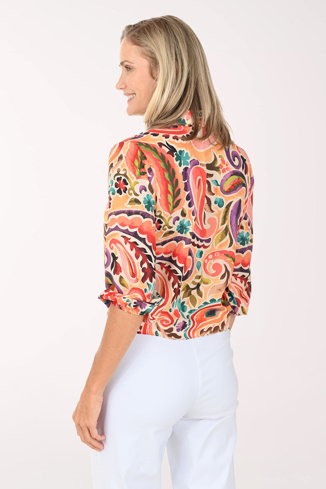 Woman wearing a colorful paisley blouse and white pants on a white background