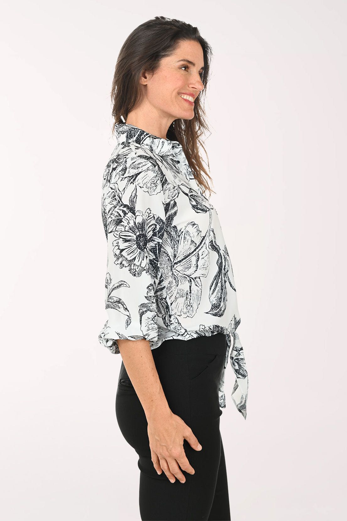 Woman wearing a black and white floral blouse with a tie waist on a white background