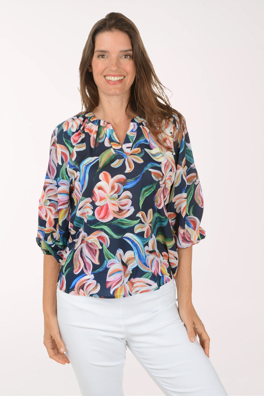 Woman wearing a colorful floral blouse with white pants on a white background