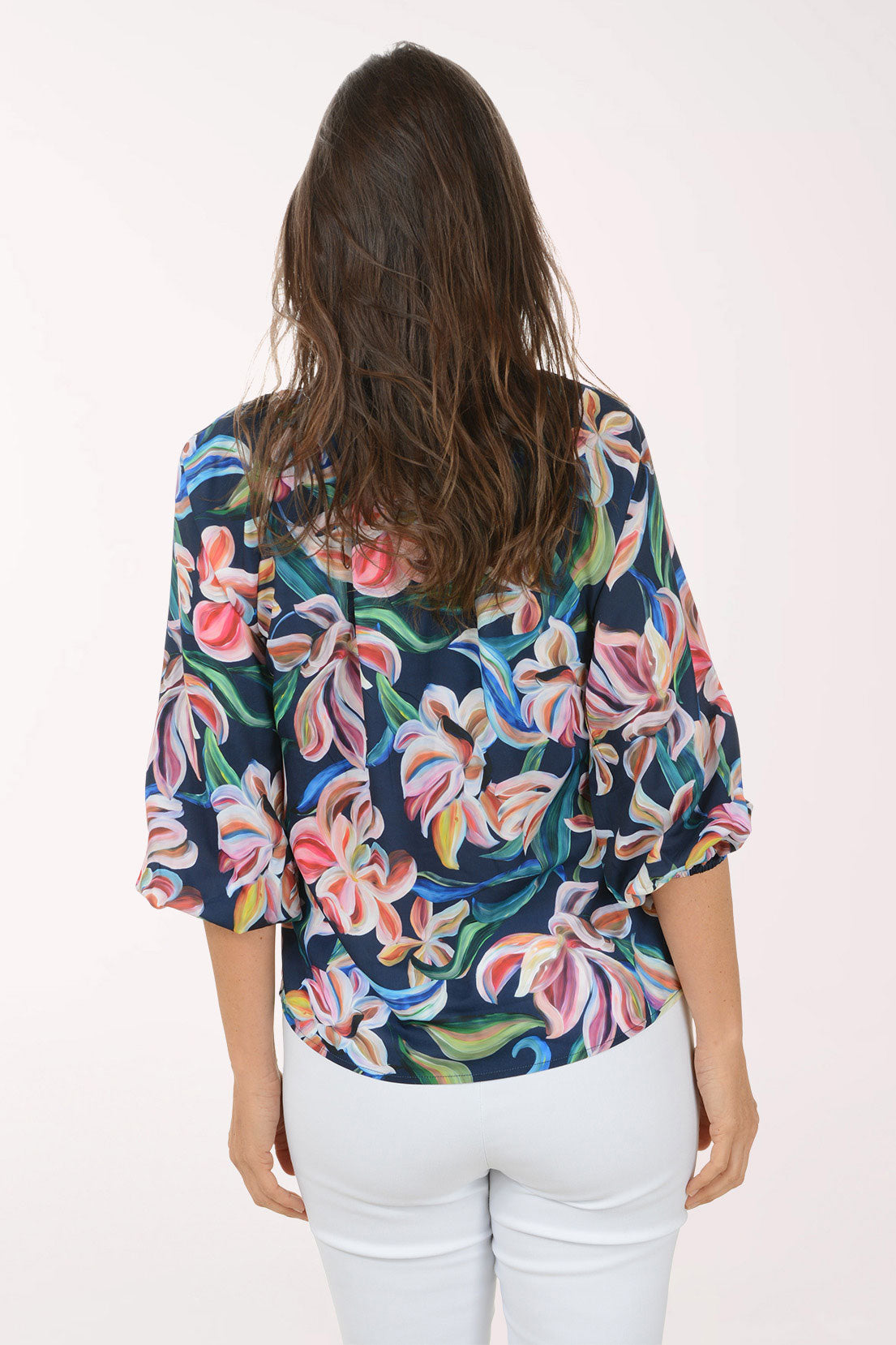 Woman wearing a colorful floral blouse with white pants on a white background