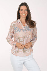 Woman wearing a floral blouse and white pants on a light pink background