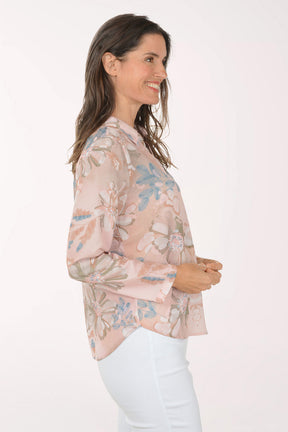 Woman wearing a floral blouse and white pants on a light pink background