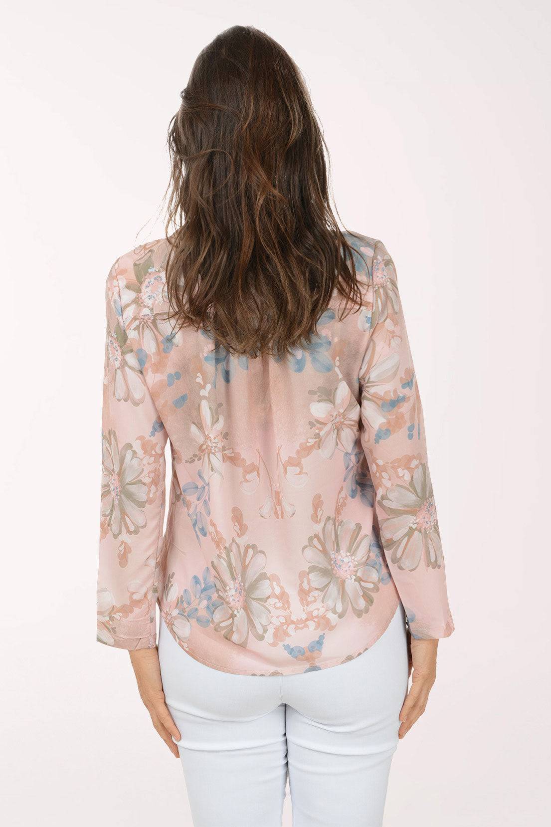 Woman wearing a floral blouse and white pants on a light pink background