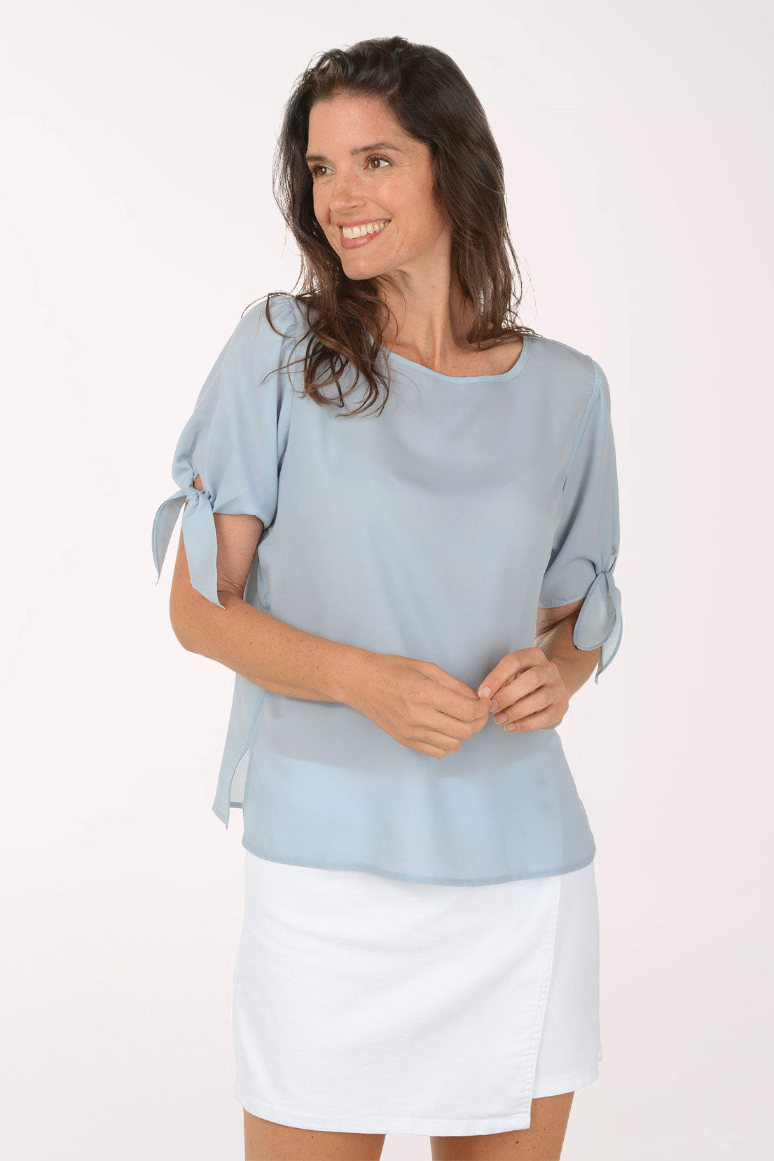 Woman wearing a light grey blouse with rolled-up sleeves and a white skirt on a white background