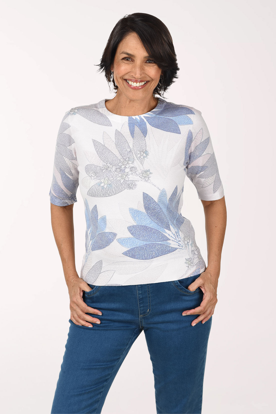 Woman wearing a white and blue patterned top with blue jeans on a white background