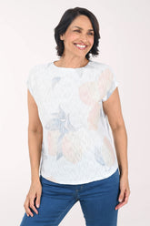 Woman wearing a light-colored floral sweater with blue pants on a white background