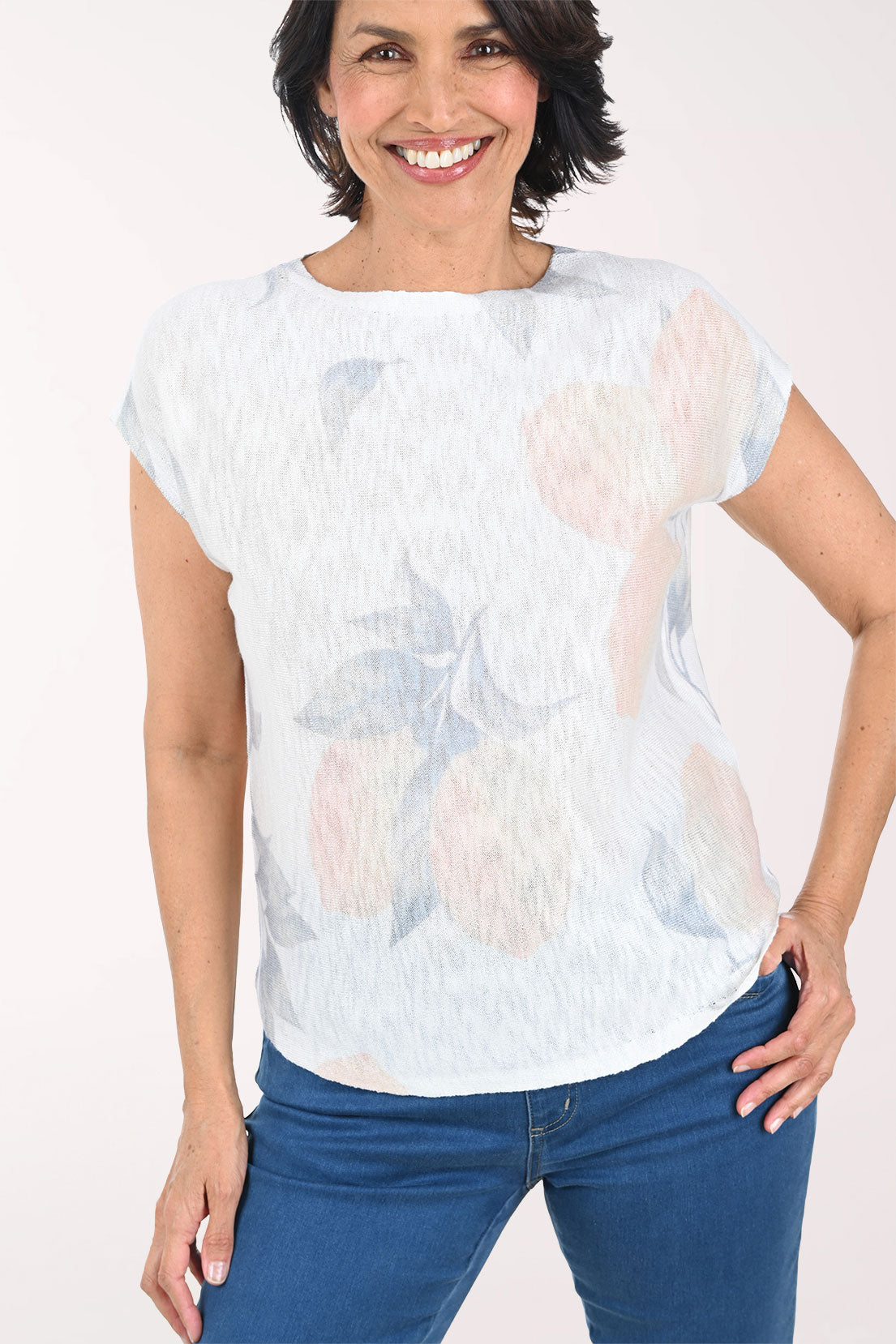 Woman wearing a light-colored floral sweater with blue pants on a white background