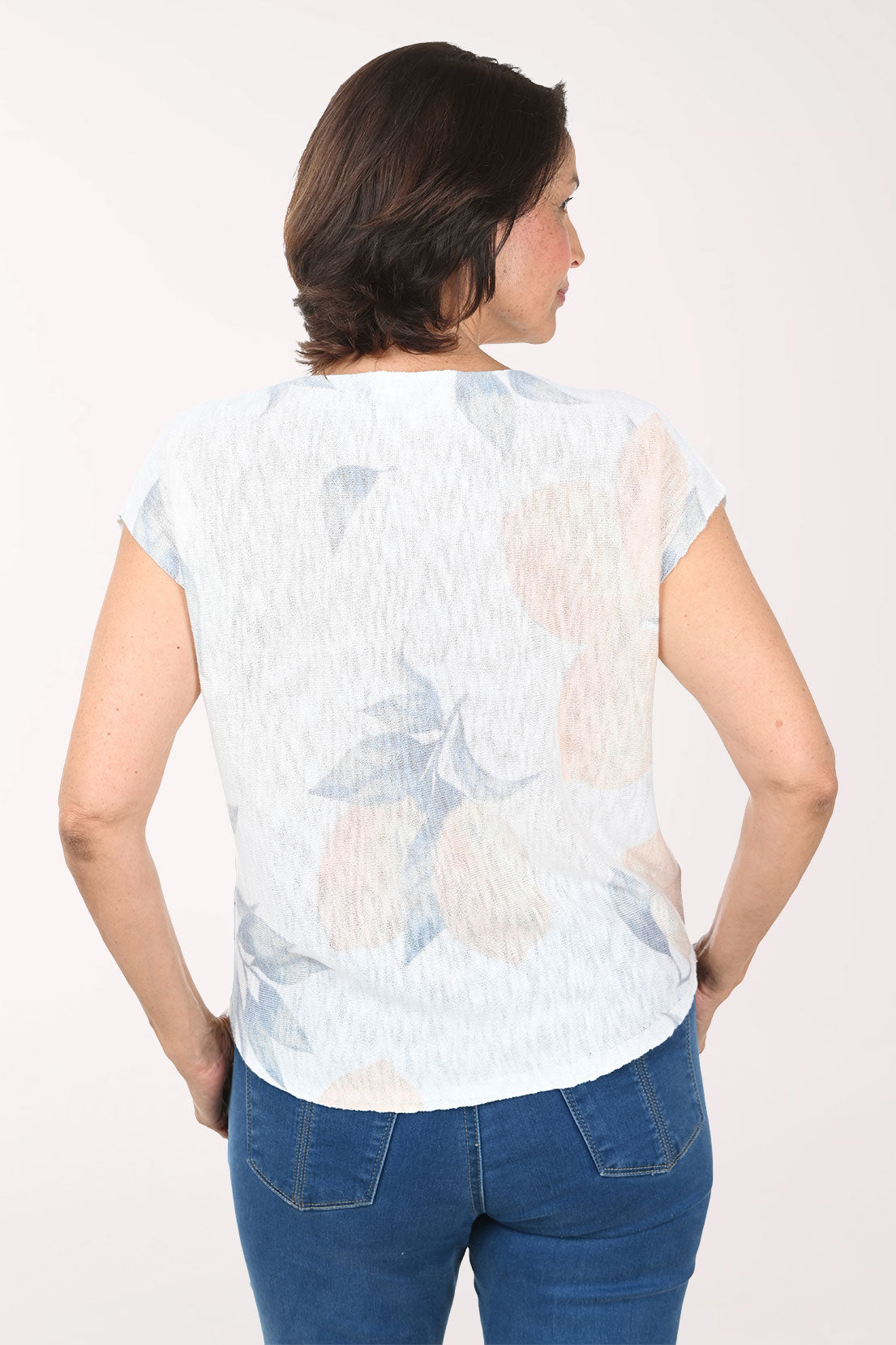 Woman wearing a light-colored floral sweater with blue pants on a white background