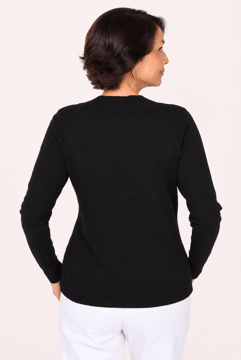 A woman shown from the back wearing a black long-sleeve knit sweater and white pants against a plain light background.