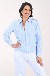 Woman wearing a light blue striped shirt and white pants on a plain background