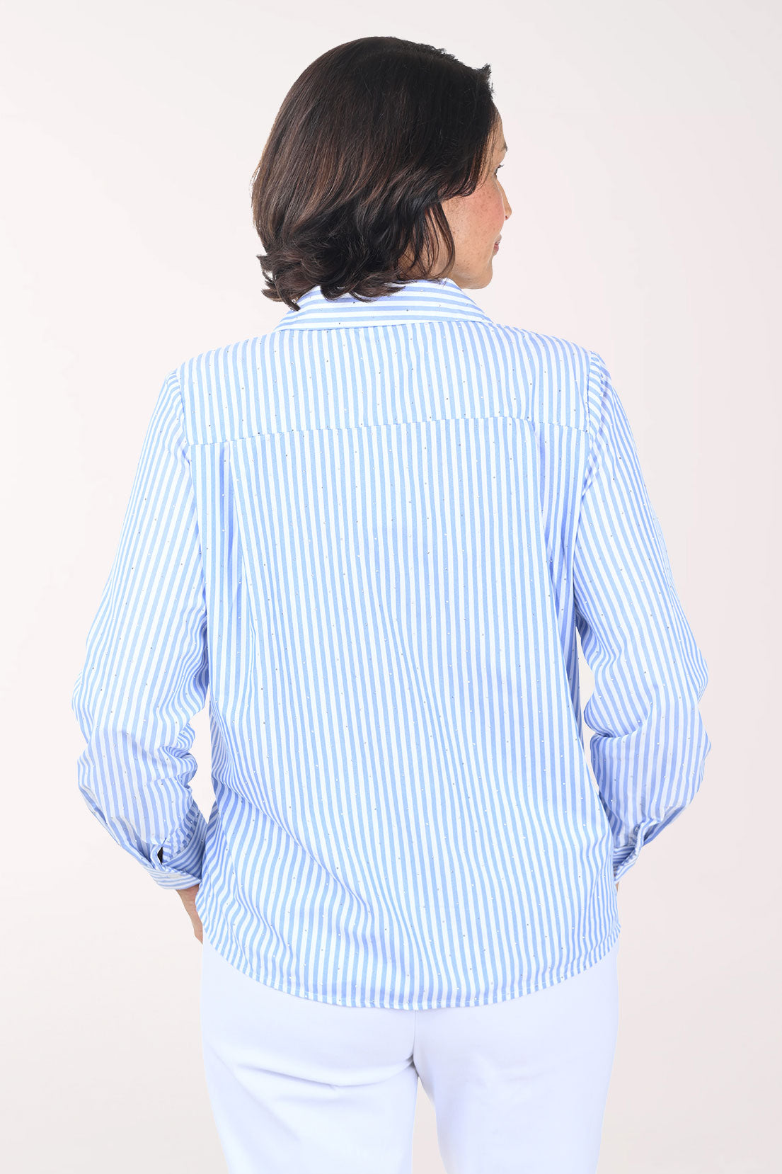 Woman wearing a light blue striped shirt and white pants on a plain background