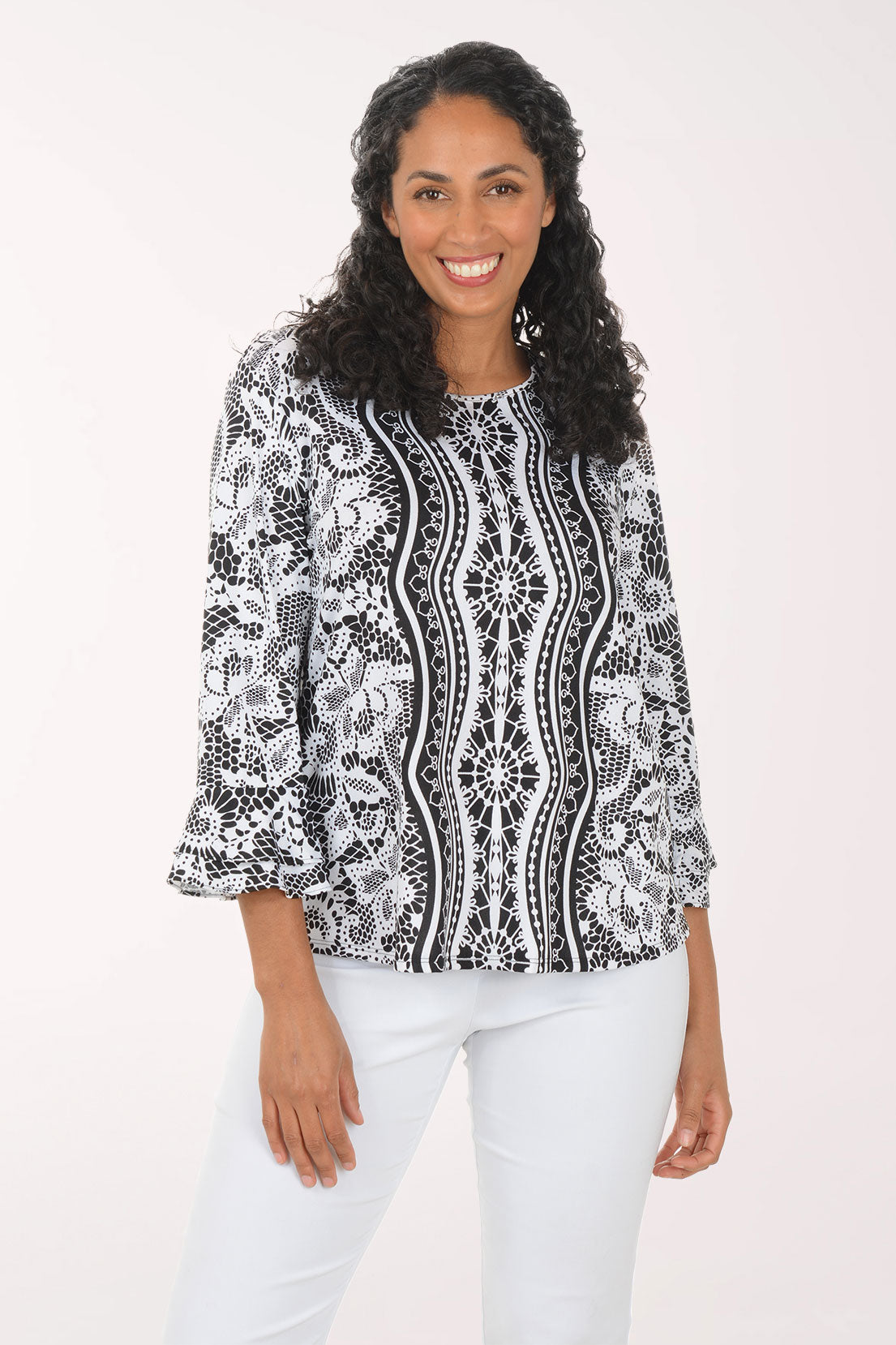 Woman wearing a black and white patterned blouse with white pants on a white background