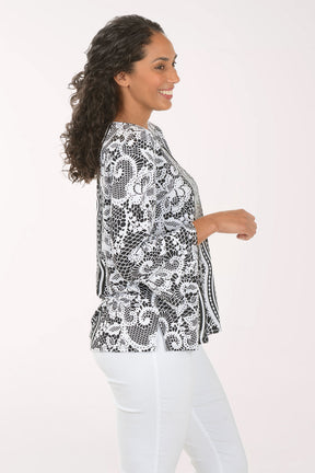 Woman wearing a black and white patterned blouse with white pants on a white background