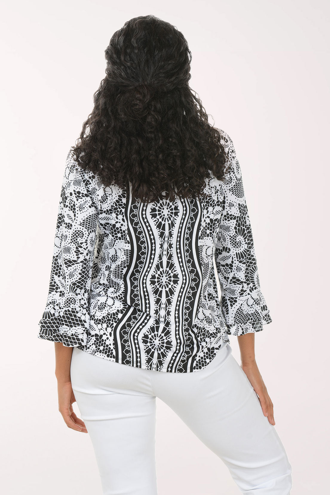 Woman wearing a black and white patterned blouse with white pants on a white background