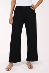 A person wearing black  wide-leg pants with an elastic waistband and side pockets, paired with a white top and flat sandals, photographed against a plain light background.