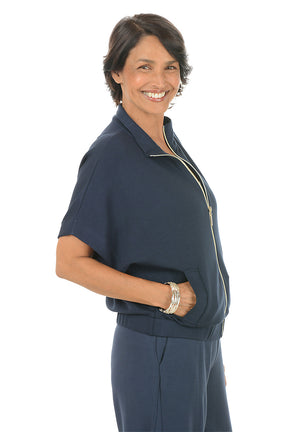 Woman wearing a navy blue zip-up top with a white background. Side shot.