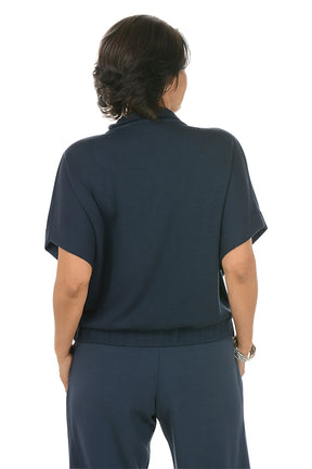 Woman wearing a navy blue zip-up top with a white background. Back shot.