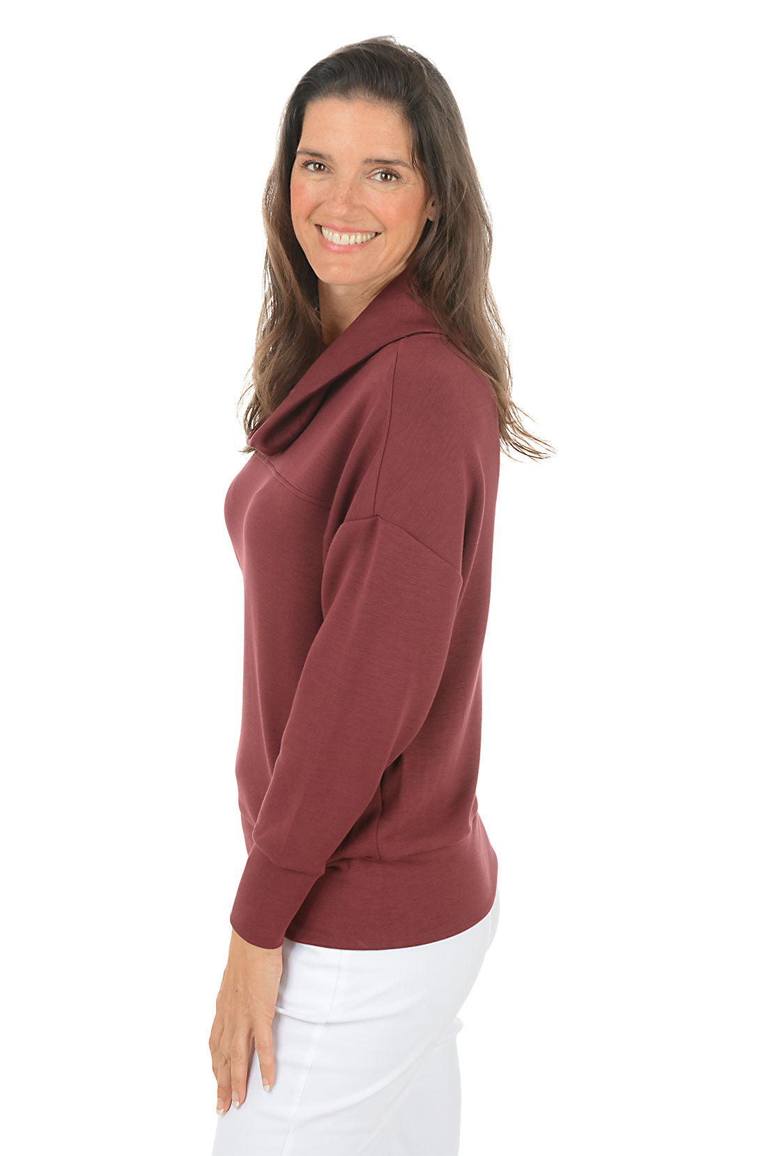 Woman wearing a maroon cowl-neck sweater and white pants on a white background. Side shot.