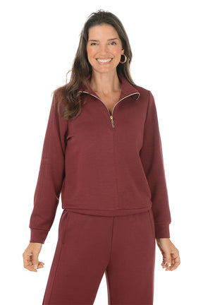 Woman wearing a maroon pullover sweater with a zipper on a white background.