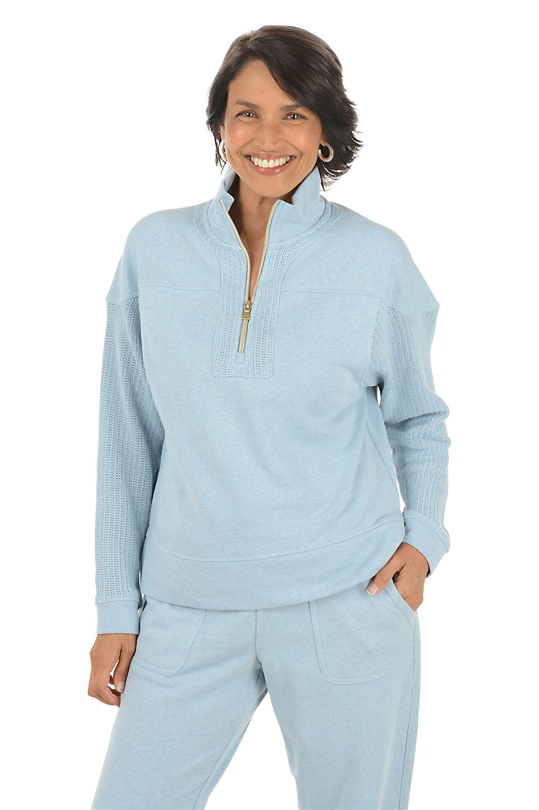 Woman wearing a light blue pullover with a quarter zip and matching pants on a white background