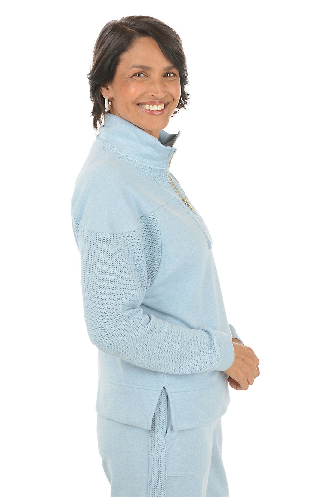 Woman wearing a light blue pullover with a quarter zip and matching pants on a white background. Side shot.