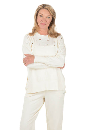 Woman wearing a cream sweatshirt with embellishments on a white background