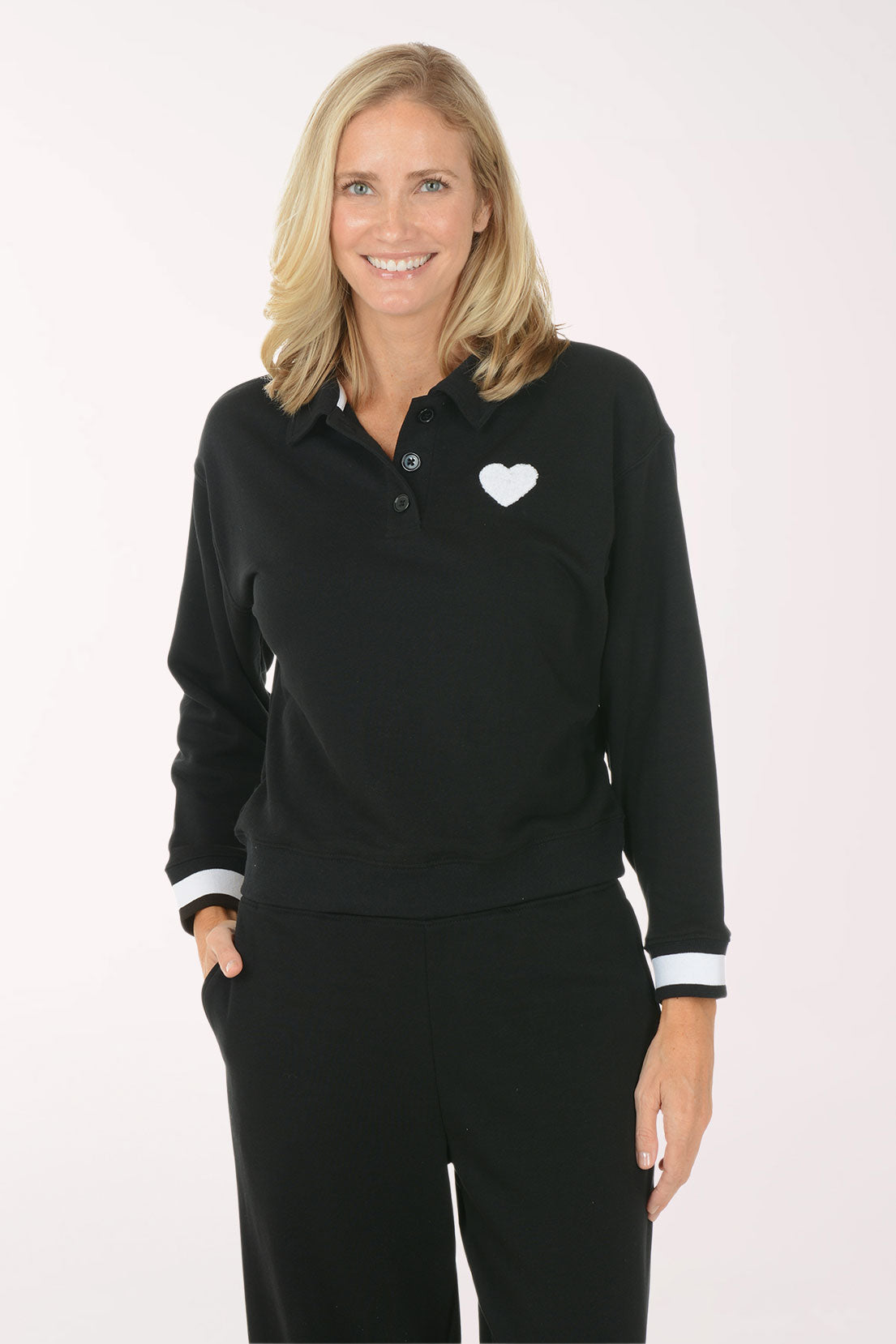 Woman wearing a black long-sleeve polo shirt with a white heart emblem on a white background