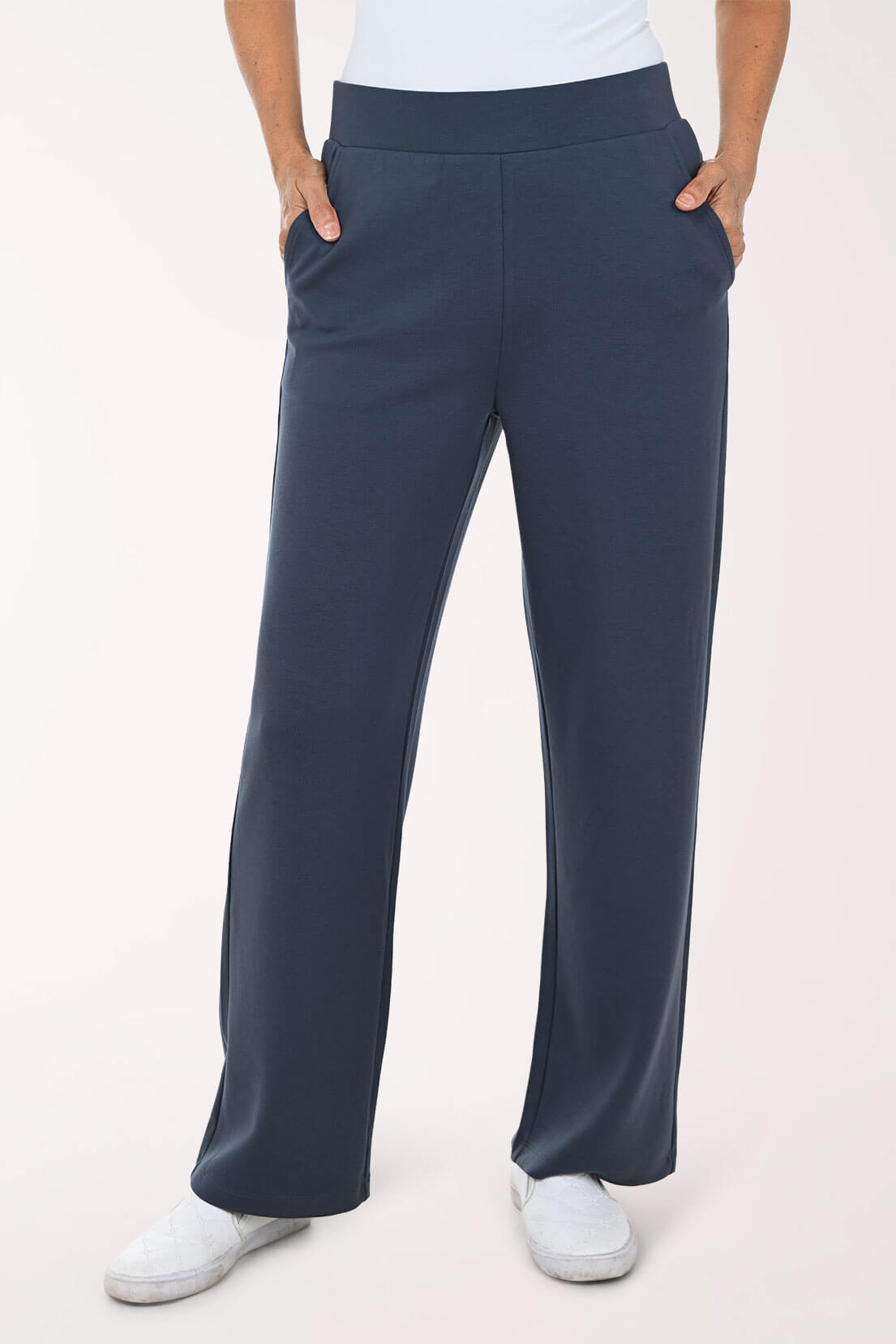 A person wearing navy wide-leg pants with side pockets, paired with a white top and white slip-on shoes, shown from the waist down against a light studio background.