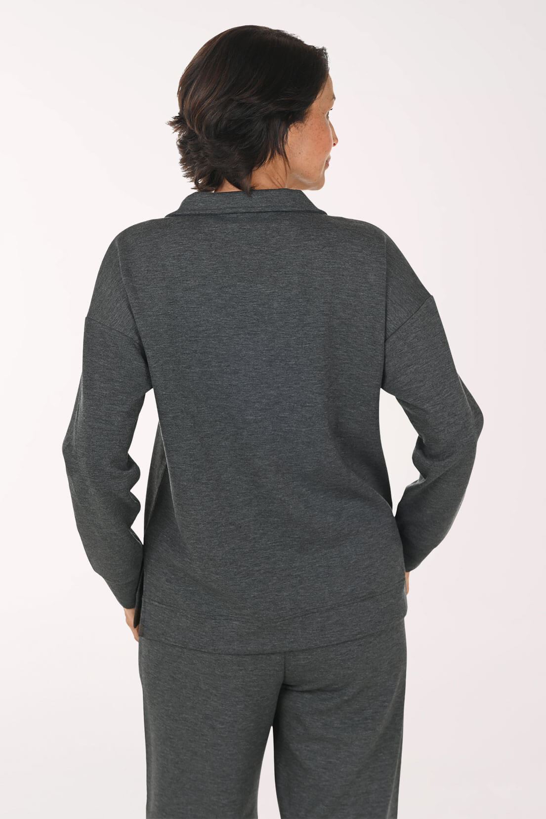 Woman wearing a dark gray long-sleeve polo-style top and matching dark gray pants, standing against a plain light background.