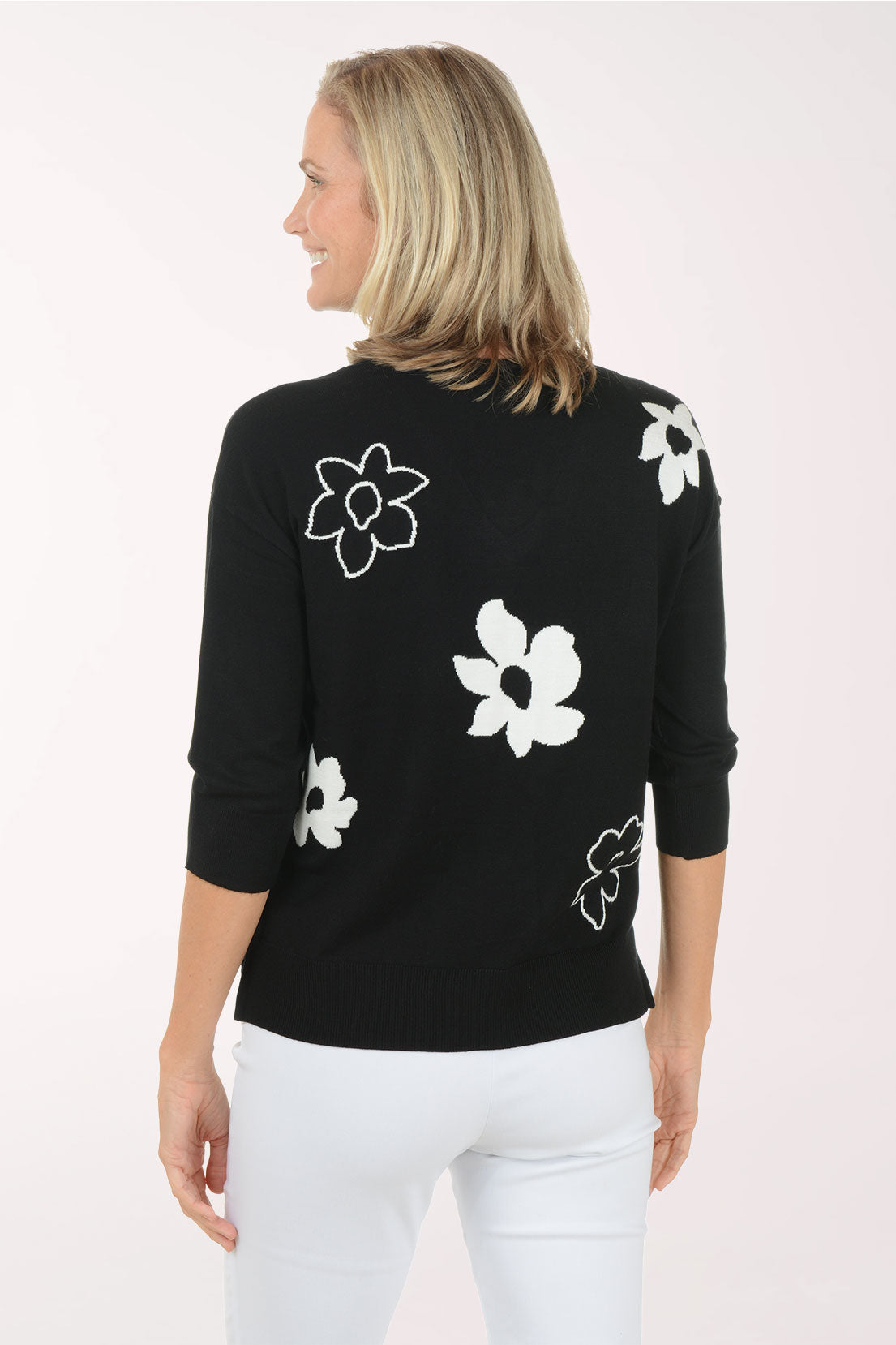 Woman wearing a black sweater with white floral patterns on a white background