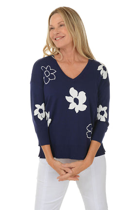 Woman wearing a navy blue sweater with white floral patterns on a white background.