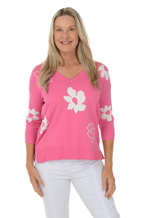 Woman wearing a pink sweater with white floral patterns on a white background.