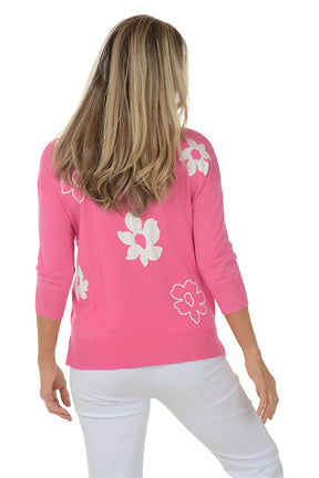 Woman wearing a pink sweater with white floral patterns on a white background. Back shot.