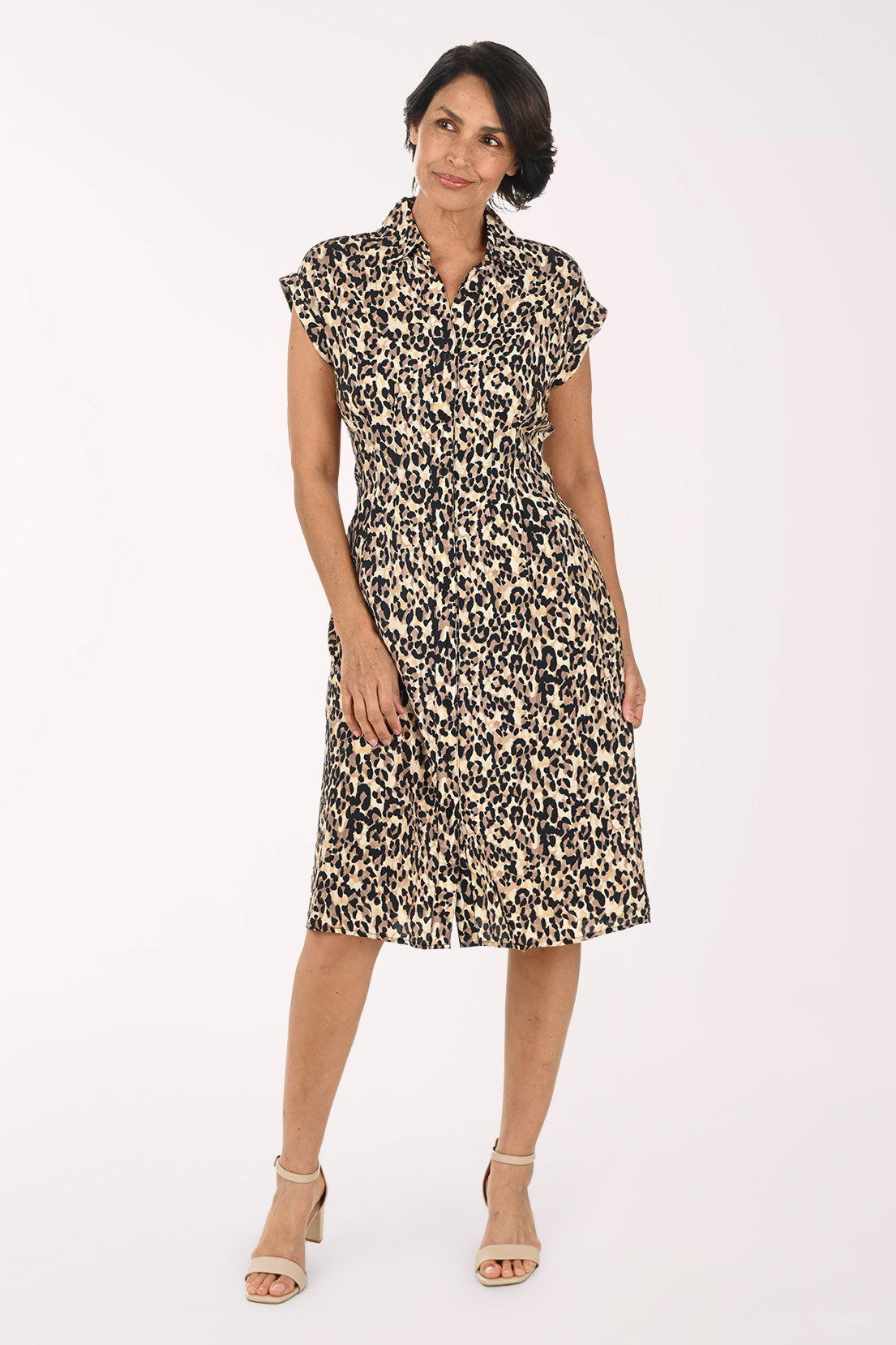 A woman modeling a short-sleeve collared dress with a beige, brown, and black leopard print pattern, paired with beige heeled sandals, against a plain white studio background.