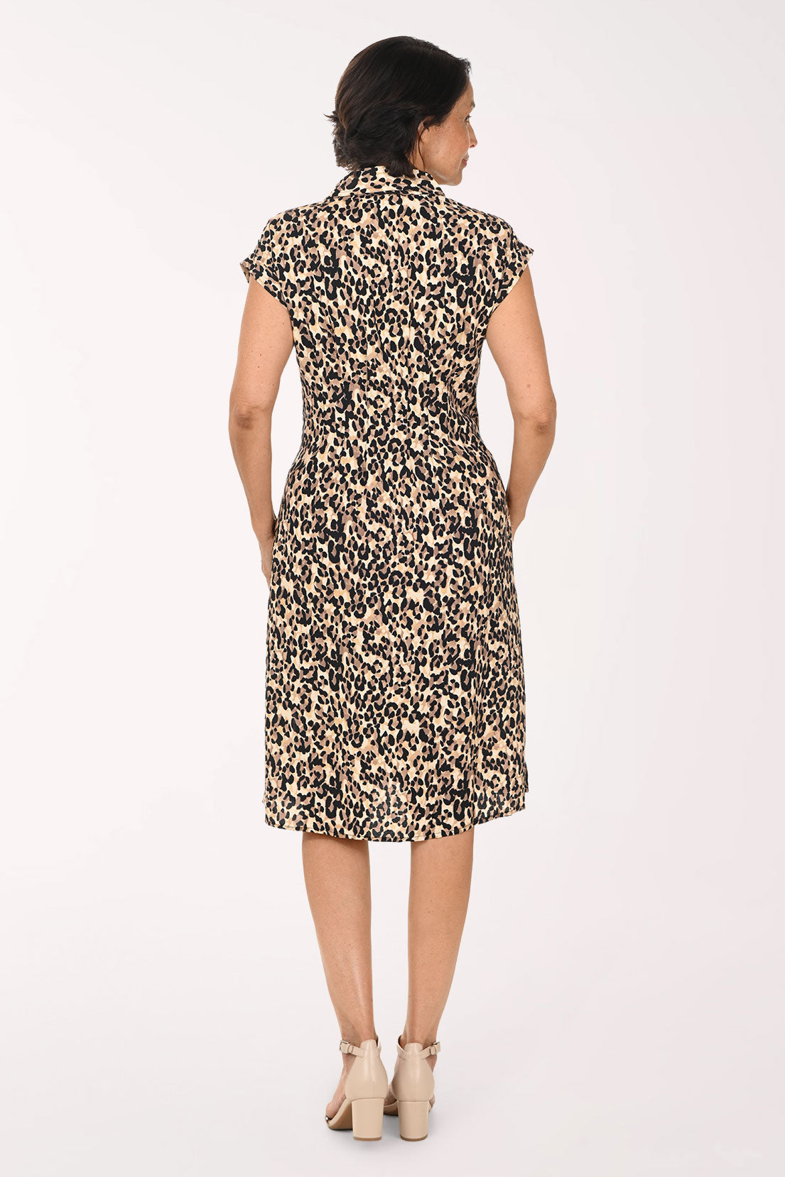 A woman modeling a short-sleeve collared dress with a beige, brown, and black leopard print pattern, paired with beige heeled sandals, against a plain white studio background.