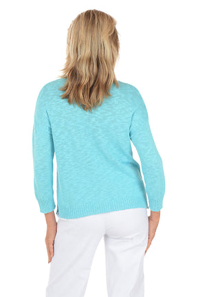 Woman wearing a light blue sweater with a palm tree design on a white background. Back shot.