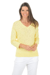 Woman wearing a yellow sweater and white pants on a white background.