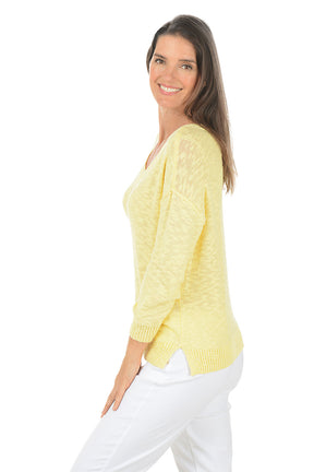 Woman wearing a yellow sweater and white pants on a white background. Side shot.