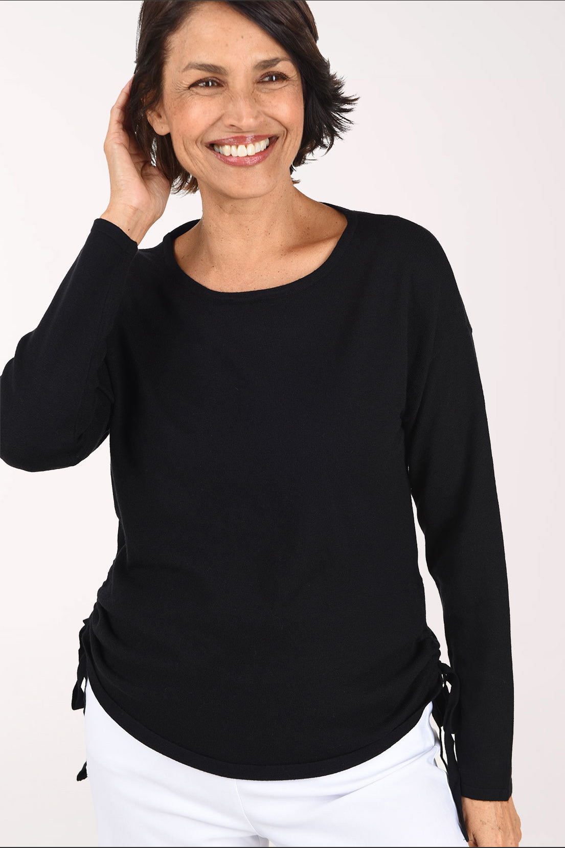 Front view of the black sweater, showing the drop shoulders, long sleeves and ties at the ruched sides of the curved hem
