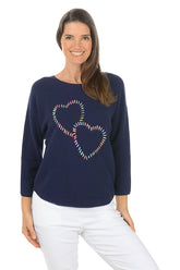 Woman wearing a navy sweater with a colorful heart design on a white background.