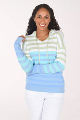 Front view of a woman smiling in the Ninety Clothing Sky Gradient Striped Hoodie, with sage and white stripes at the top fading to aqua and periwinkle, worn with white jeans.