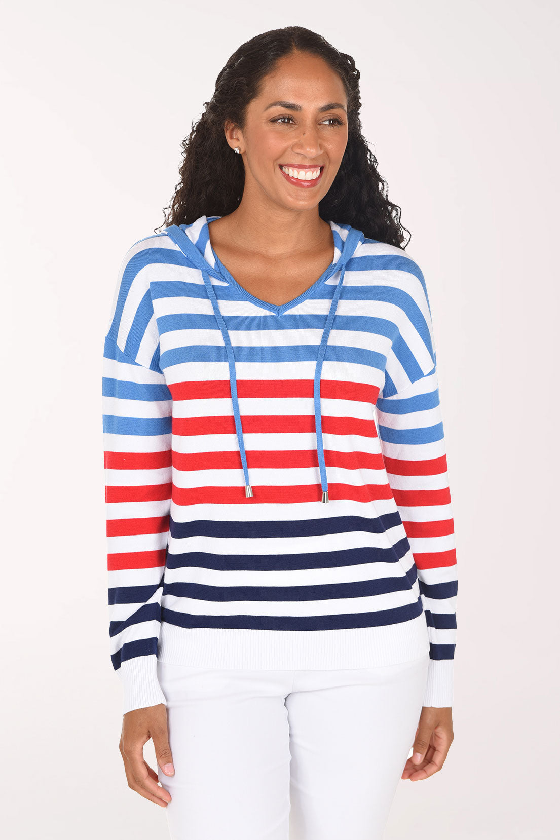 Front view of a woman smiling in the Ninety Clothing Red White Blue Striped Hoodie, with blue, red and navy stripes on white, a drawstring hood and white jeans.
