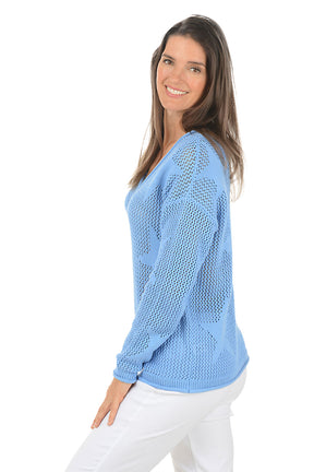 Woman wearing a light blue sweater and white pants on a white background. Side shot.